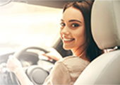 Foto de uma mulher sorridente sentada ao volante de um carro, olhando para trás
